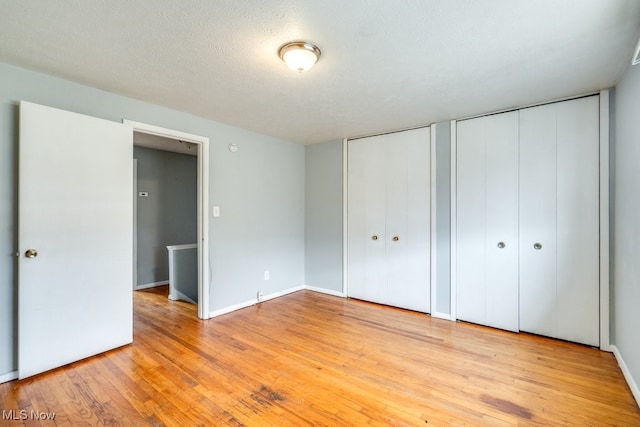 unfurnished bedroom with baseboards, multiple closets, and light wood-type flooring