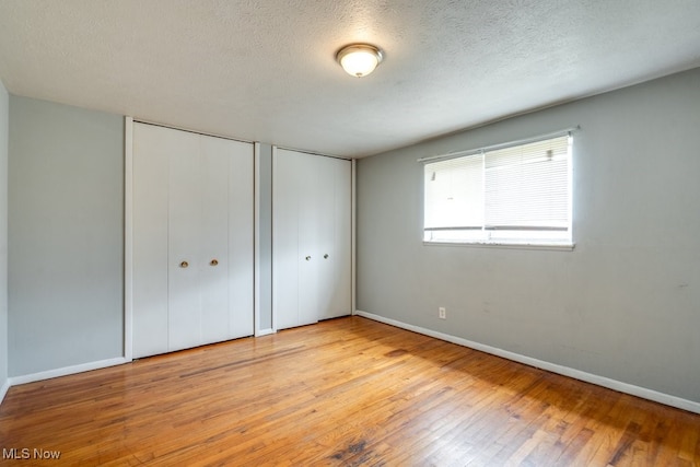unfurnished bedroom with two closets, a textured ceiling, baseboards, and hardwood / wood-style floors