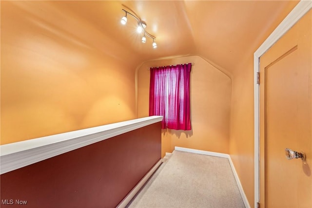 corridor featuring baseboards, vaulted ceiling, and carpet flooring