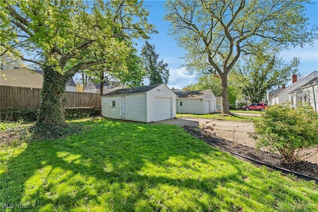 view of yard featuring driveway, fence, an outdoor structure, and a garage