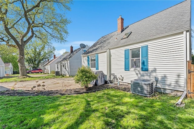back of house featuring a lawn, a chimney, and cooling unit