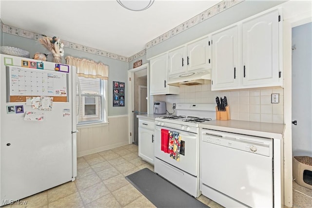 kitchen with white appliances, light countertops, white cabinetry, under cabinet range hood, and a wainscoted wall