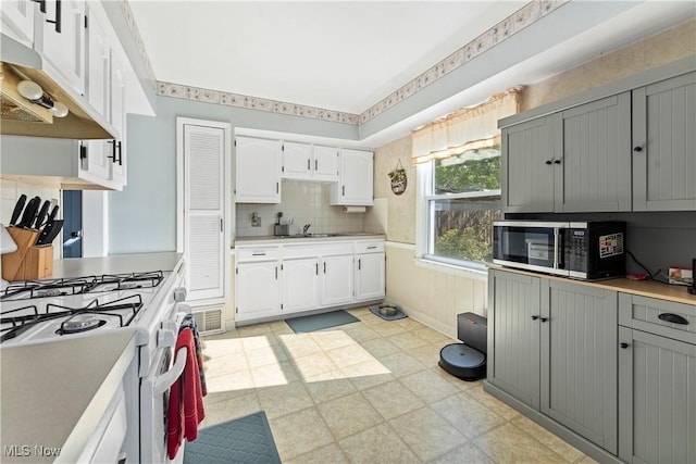 kitchen featuring white gas stove, stainless steel microwave, light floors, under cabinet range hood, and white cabinetry