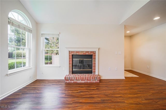 unfurnished living room featuring baseboards, a brick fireplace, wood finished floors, and a healthy amount of sunlight
