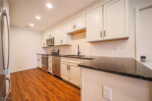 kitchen with dark wood-style flooring, appliances with stainless steel finishes, a sink, dark stone countertops, and recessed lighting