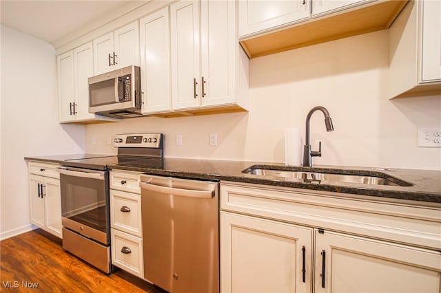 kitchen with appliances with stainless steel finishes, a sink, dark stone countertops, white cabinetry, and dark wood-style floors