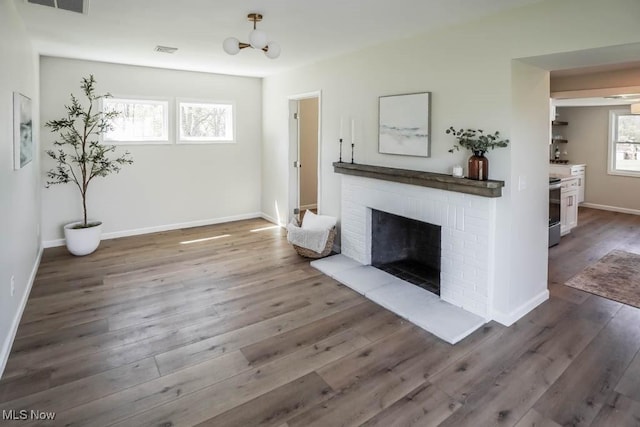 unfurnished living room featuring visible vents, a brick fireplace, wood finished floors, baseboards, and a notable chandelier