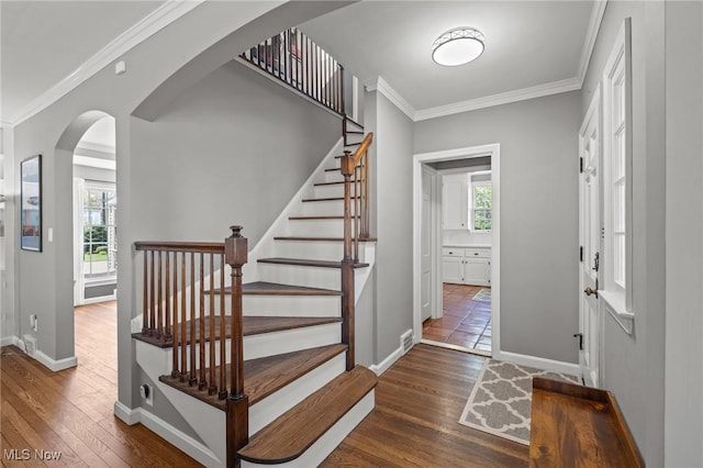 stairway with arched walkways, plenty of natural light, ornamental molding, and hardwood / wood-style floors