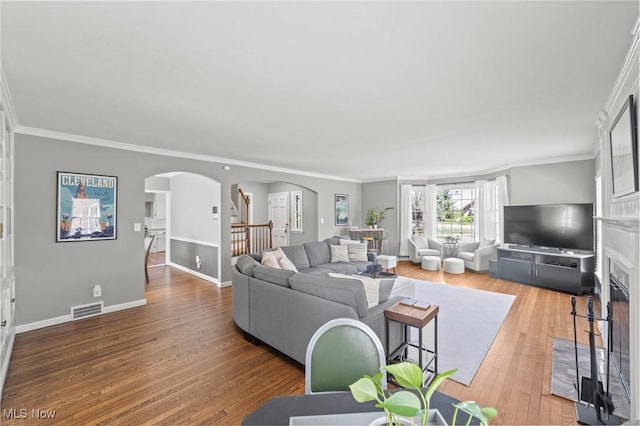 living room featuring arched walkways, visible vents, ornamental molding, and wood finished floors