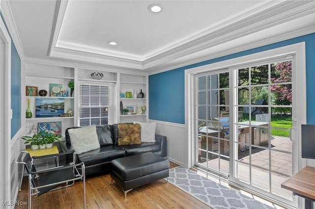 living area with built in shelves, a tray ceiling, ornamental molding, and wood finished floors