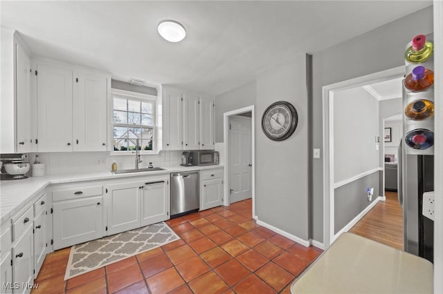 kitchen with light countertops, white cabinetry, a sink, appliances with stainless steel finishes, and backsplash
