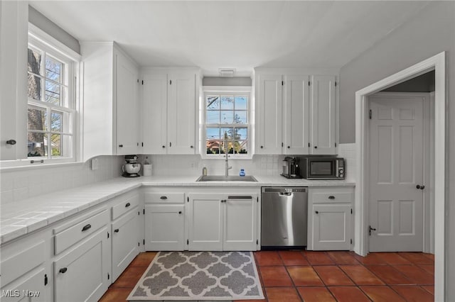 kitchen with a sink, stainless steel dishwasher, black microwave, and a wealth of natural light