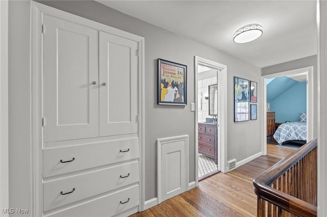 corridor featuring baseboards, a sink, and light wood-style floors