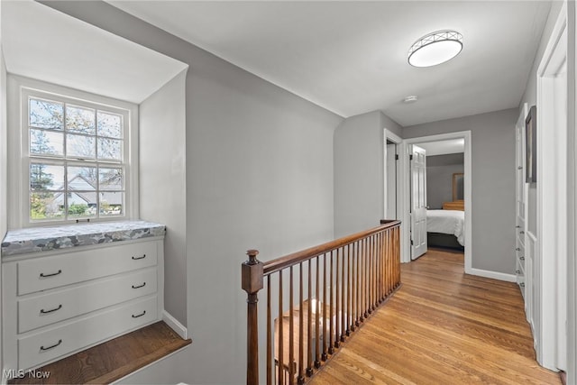 hallway featuring baseboards, an upstairs landing, and light wood-type flooring