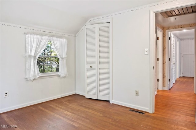 unfurnished bedroom with light wood-style floors, baseboards, lofted ceiling, visible vents, and a closet