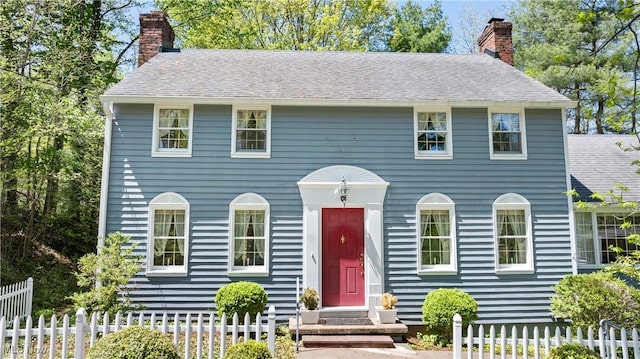 colonial house featuring fence, a chimney, and a shingled roof