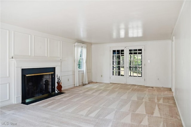 unfurnished living room featuring light colored carpet, a fireplace with flush hearth, and french doors