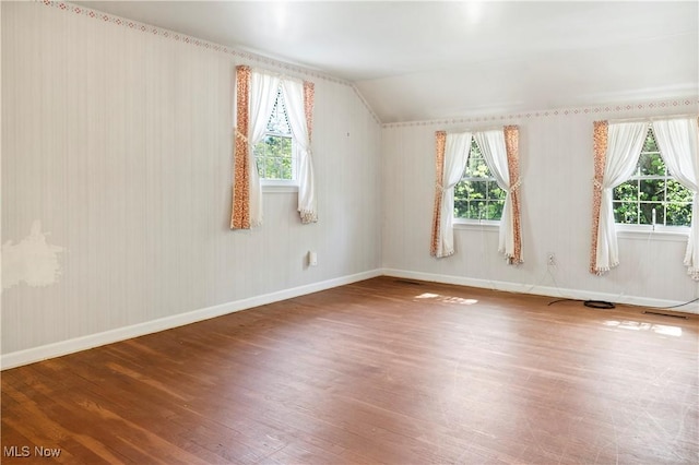 additional living space with baseboards, plenty of natural light, vaulted ceiling, and wood finished floors