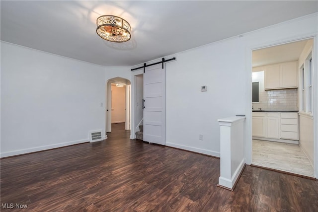 interior space with visible vents, arched walkways, a barn door, wood finished floors, and baseboards