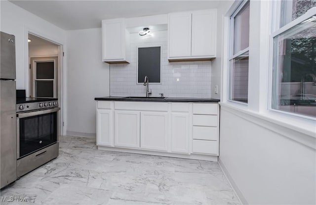 kitchen with white cabinets, a sink, marble finish floor, stainless steel appliances, and backsplash