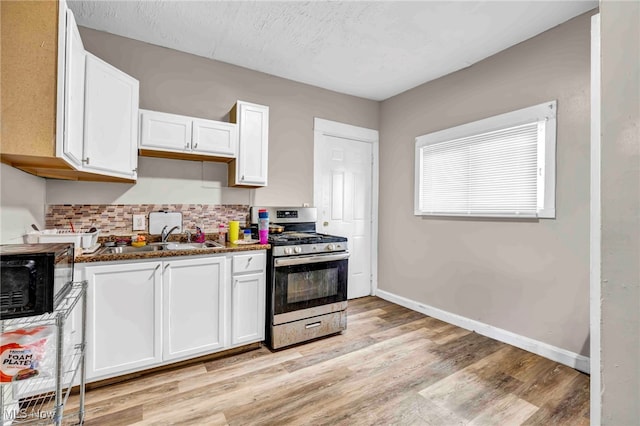 kitchen with a sink, stainless steel gas range, backsplash, and white cabinets