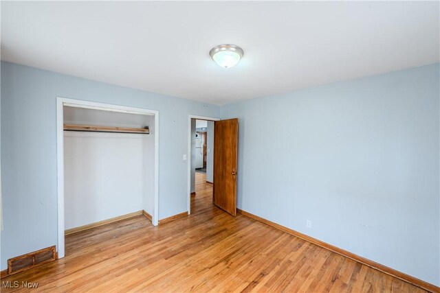 unfurnished bedroom featuring baseboards, light wood finished floors, and a closet