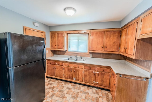 kitchen with freestanding refrigerator, brown cabinets, decorative backsplash, and a sink