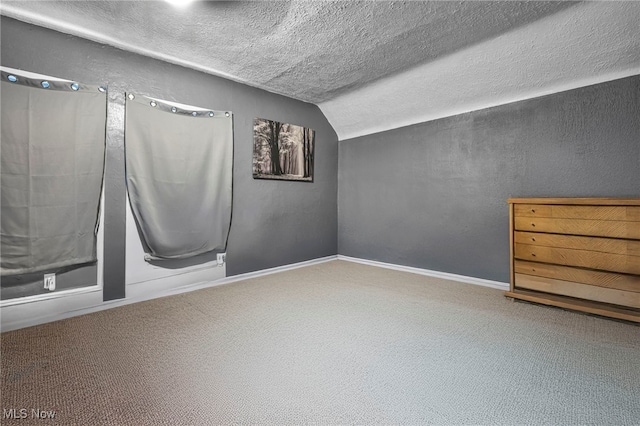 carpeted empty room with baseboards, a textured ceiling, a textured wall, and vaulted ceiling