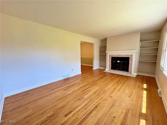 unfurnished living room featuring visible vents, baseboards, built in shelves, a tile fireplace, and light wood-style flooring