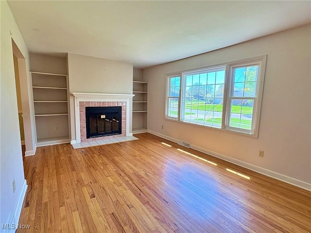 unfurnished living room featuring baseboards, visible vents, a tile fireplace, and light wood-style floors