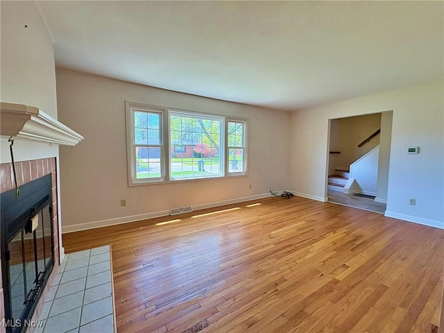 unfurnished living room with light wood finished floors, a tiled fireplace, baseboards, visible vents, and stairway