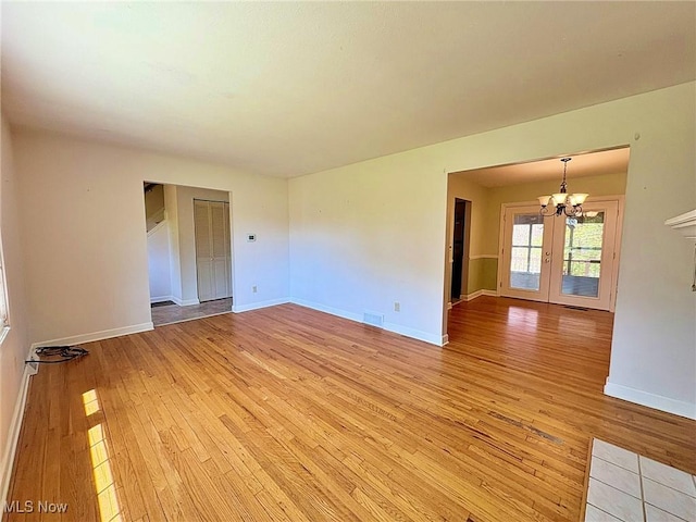 spare room featuring visible vents, light wood-style flooring, a notable chandelier, and french doors