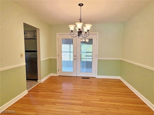 unfurnished dining area with visible vents, baseboards, a chandelier, french doors, and light wood finished floors
