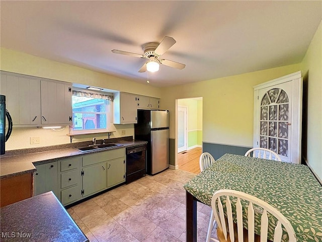 kitchen with ceiling fan, dark countertops, dishwasher, a sink, and freestanding refrigerator
