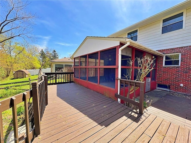 wooden deck featuring a sunroom, an outbuilding, and a storage unit
