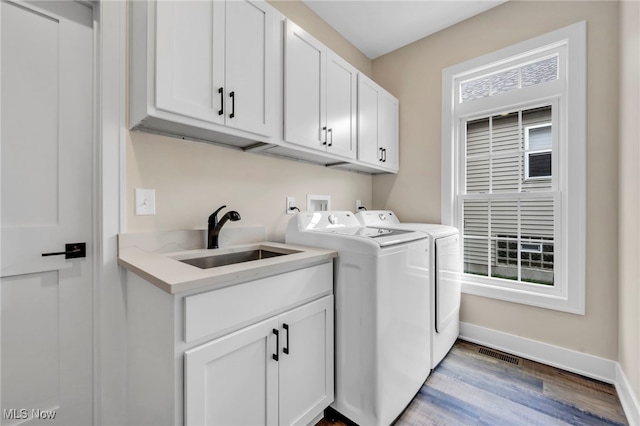 laundry room with visible vents, washing machine and clothes dryer, cabinet space, a sink, and light wood-style flooring