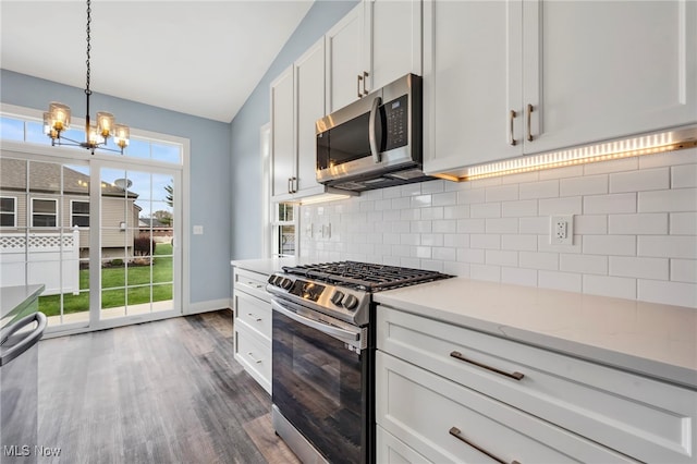 kitchen with an inviting chandelier, dark wood-style flooring, lofted ceiling, tasteful backsplash, and appliances with stainless steel finishes