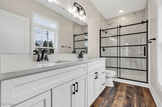 full bathroom featuring double vanity, wood finished floors, toilet, a sink, and a marble finish shower