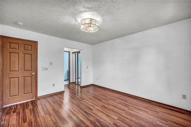 empty room featuring a textured ceiling, baseboards, and wood finished floors