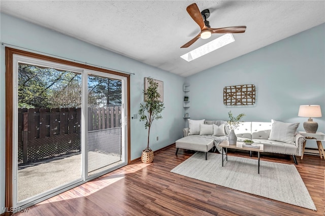 living area featuring a ceiling fan, a textured ceiling, wood finished floors, baseboards, and lofted ceiling with skylight