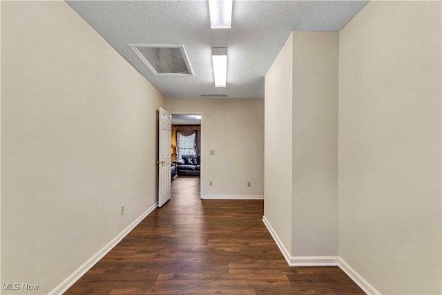corridor featuring dark wood-style flooring, a textured ceiling, visible vents, and baseboards