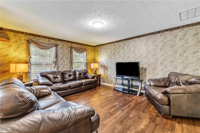 living area with a textured ceiling, wallpapered walls, visible vents, and wood finished floors