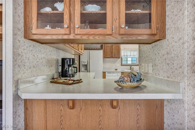 kitchen with brown cabinetry, light countertops, a peninsula, glass insert cabinets, and white appliances