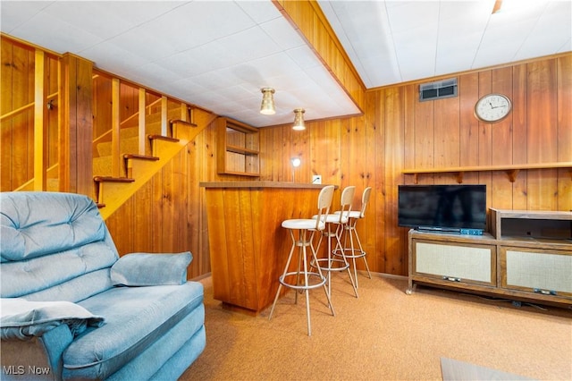 bar with visible vents, a dry bar, stairway, wooden walls, and carpet flooring