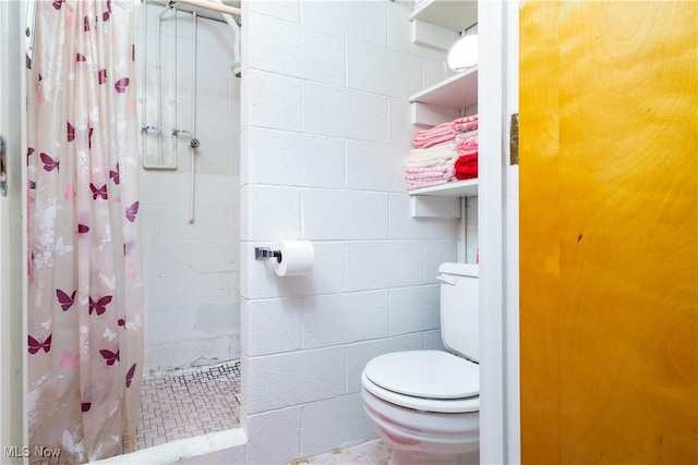 bathroom featuring toilet, concrete block wall, and a tile shower