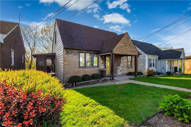 view of front facade featuring a shingled roof, a front yard, and stone siding