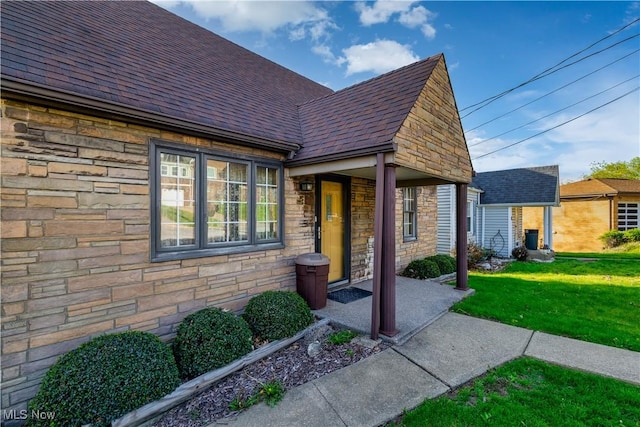 exterior space with a shingled roof, a front lawn, and stone siding