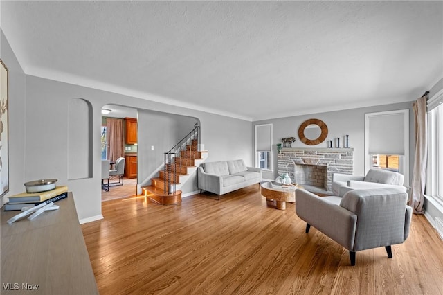 living room featuring arched walkways, stairway, a healthy amount of sunlight, and light wood finished floors