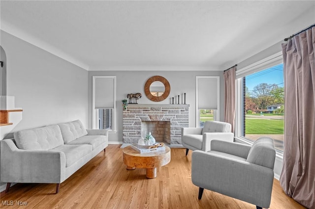 living area with arched walkways, a stone fireplace, and wood finished floors