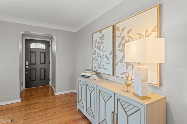 entrance foyer with arched walkways, baseboards, and light wood-type flooring